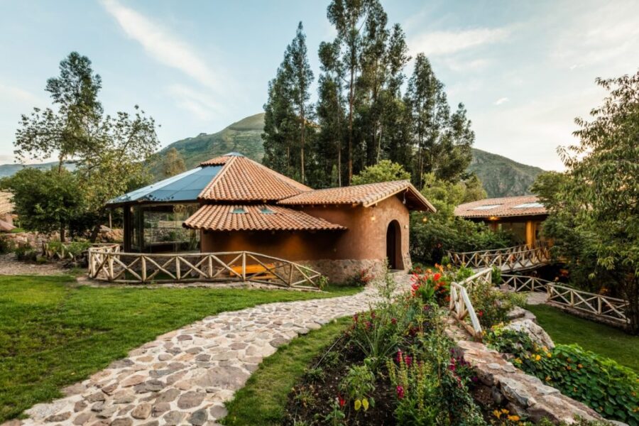 Rustic mountain yoga retreat lodge with adobe cottage, garden path, flowers, and forest backdrop.