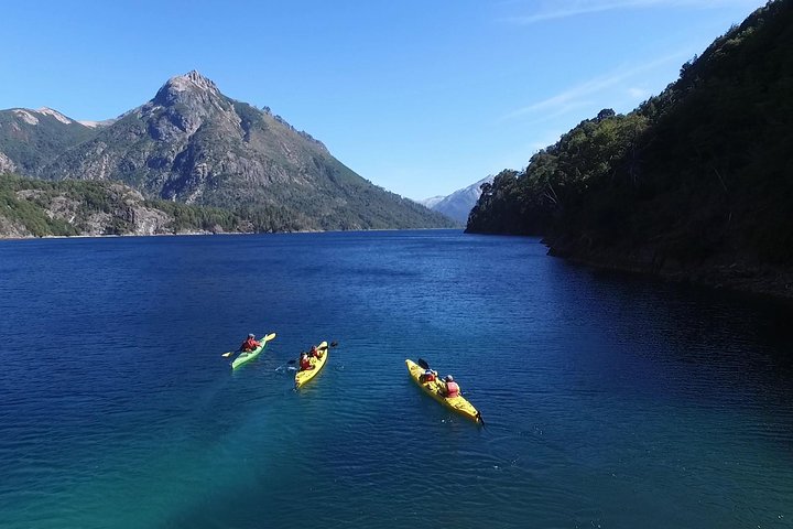 Kayakers paddling on a mountain lake in Patagonia surrounded by forested slopes and rugged peaks.