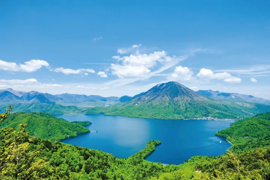 Scenic Chuzenji Onsen mountain lake panorama with lush green forest, blue water and clear sky.