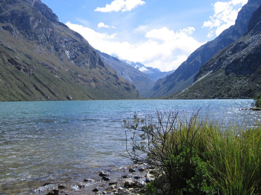 Scenic alpine mountain lake valley with turquoise water, rocky slopes, distant snow-capped peaks, and blue sky.