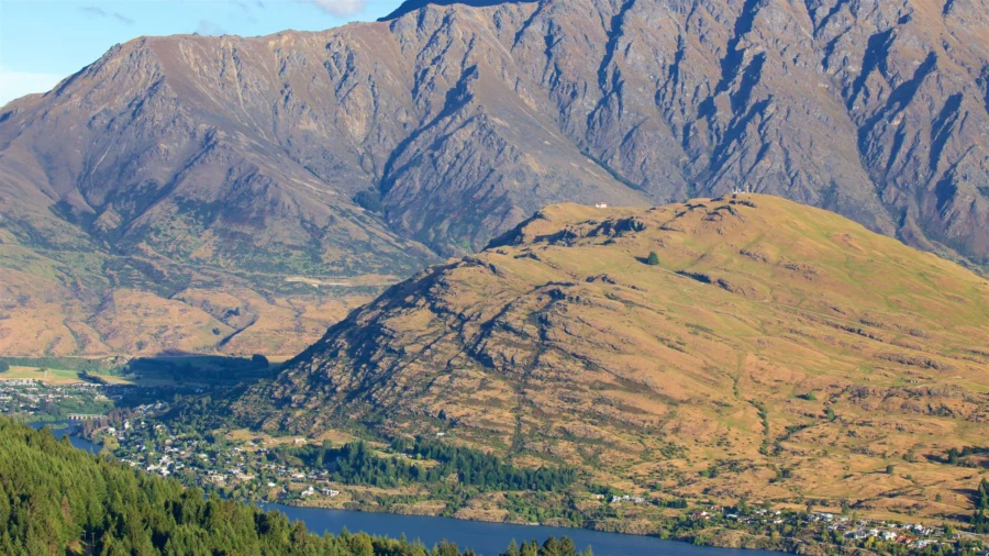 Frankton mountain village by lake with evergreen forest, golden hillside, dramatic alpine peaks landscape.