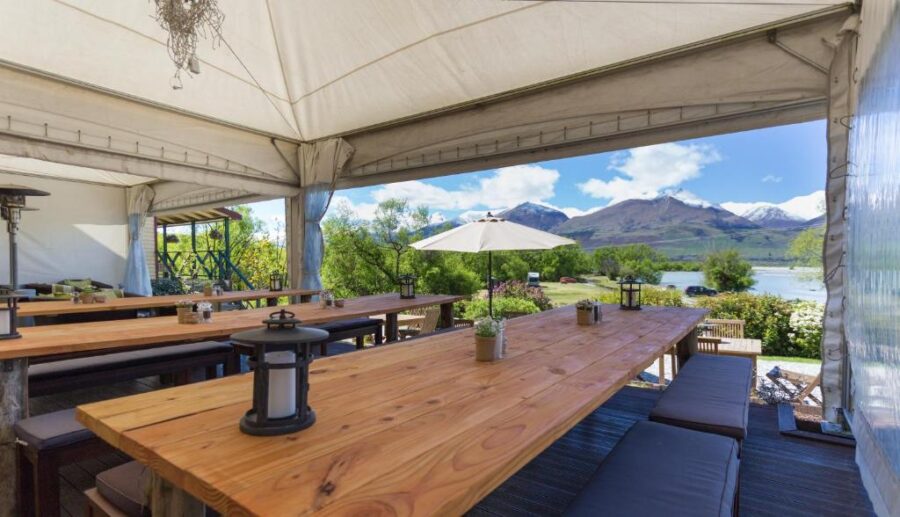 Lakeside mountain restaurant patio with covered rustic wooden tables, benches, garden views, and scenic landscape.