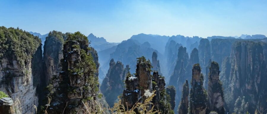 Panoramic view of rugged mountain peaks with greenery and clear blue sky backdrop.
