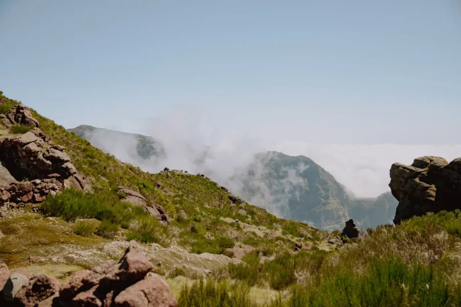 Breathtaking mountainous landscape with boulders, greenery, and misty peaks under a clear blue sky.