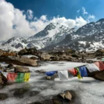 Majestic snowy mountains, serene stream, colorful prayer flags; natures beauty and cultural symbolism.