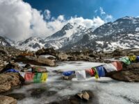 Majestic snowy mountains, serene stream, colorful prayer flags; natures beauty and cultural symbolism.