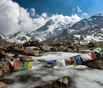 Majestic snowy mountains, serene stream, colorful prayer flags; natures beauty and cultural symbolism.