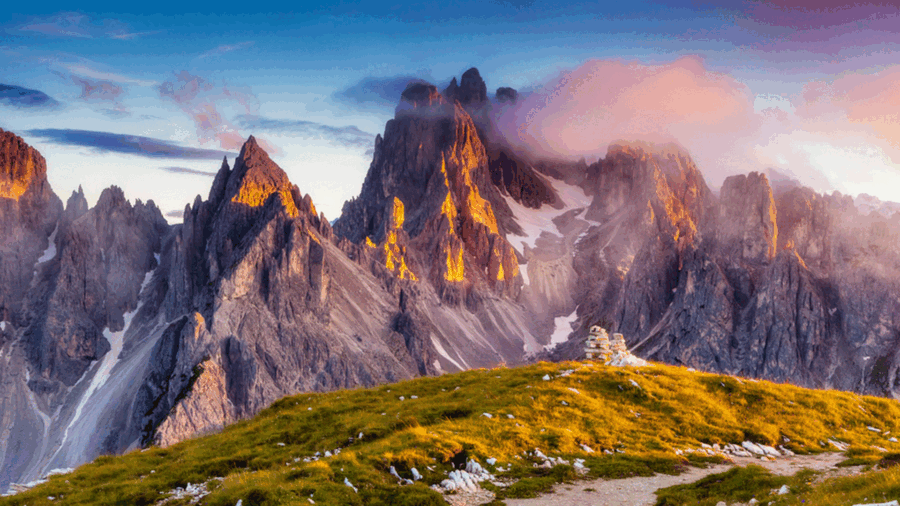Dolomites mountain sunrise with rocky peaks, lush greenery, and scenic hiking path.