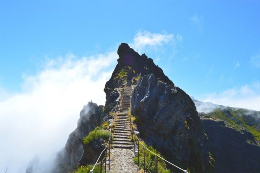 Mountain hiking path with cobblestones, rocky peak, green foliage, and blue sky in Madeira.
