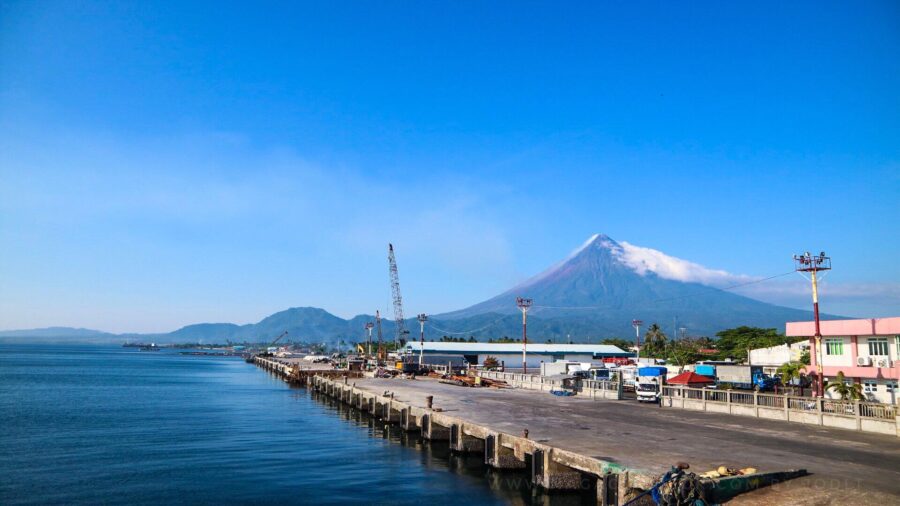 Tabaco Port pier with conical mountain backdrop, dock cranes, trucks, and calm bay.