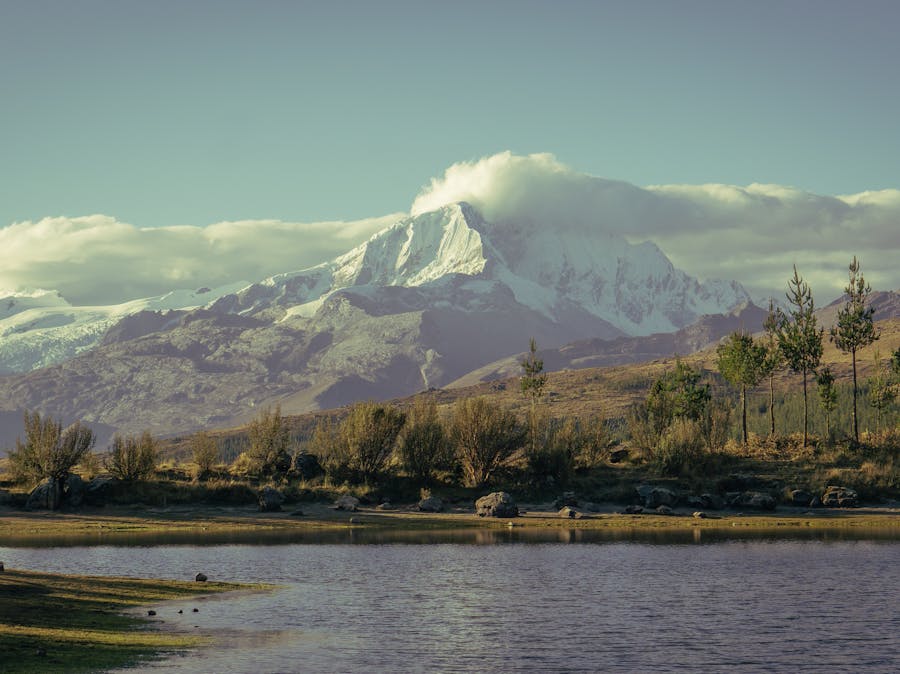 Majestic snow-capped mountain mirrored in tranquil lake with lush greenery.