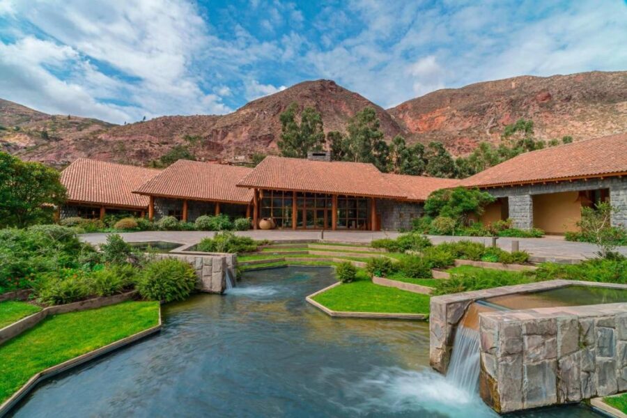 Luxury Sacred Valley mountain resort with stone courtyard, reflecting pools, waterfall stream, and Andean backdrop.