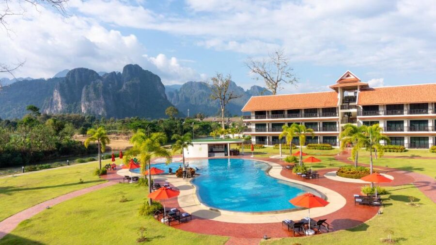 Luxury Vang Vieng mountain resort with infinity pool, palm trees, and modern hotel building.