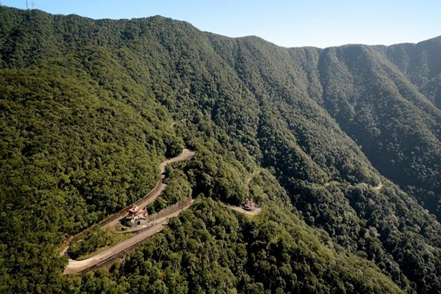 Aerial view of winding mountain road with hairpin turns through dense green forest.