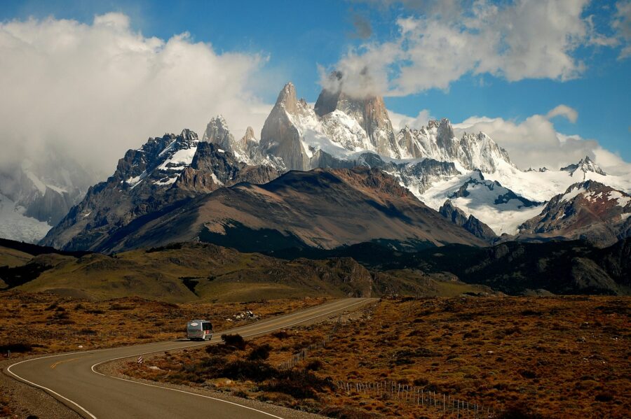 Scenic Patagonia mountain road with camper van, dramatic snowy peaks, blue sky and rugged landscape.