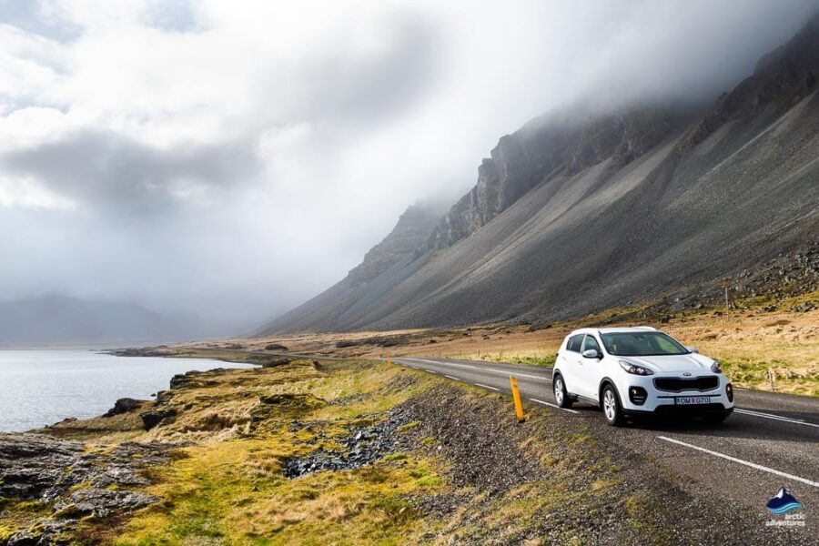 Sleek white car on coastal mountain road under dramatic clouds. Adventure and exploration scenery.