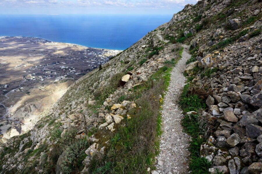 Stunning mountainous landscape overlooking serene coastline with hiking path in Santorini.
