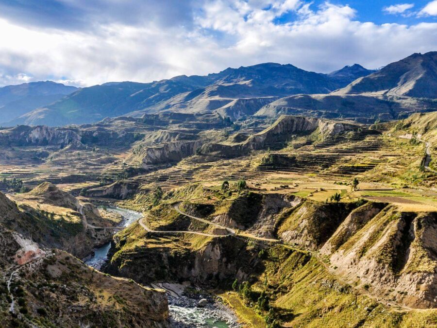 Dramatic Colca Canyon mountain landscape with terraced fields, winding river, steep cliffs and clouds.