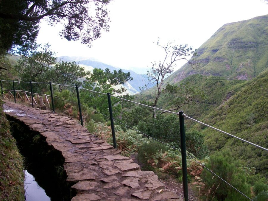 Mountain path with green railing, lush valley, and cliffs; perfect for hiking in Portugal.