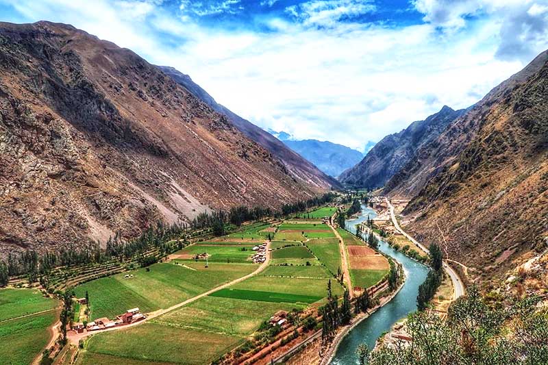 Scenic Sacred Valley mountain landscape with river, terraced farmland, rural village and Andean peaks.