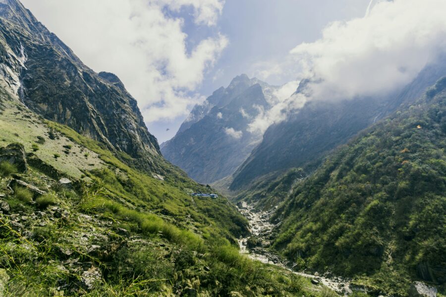Majestic mountains and serene valley with river, lush greenery, and distant clouds.