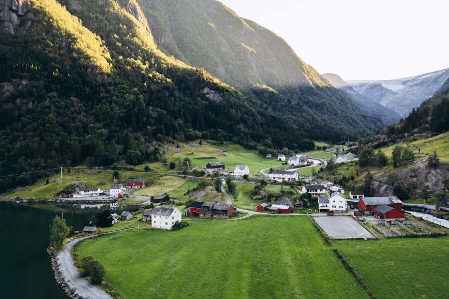 Mountain valley village with waterfront houses, green pastures, conifer forests and distant glacier.