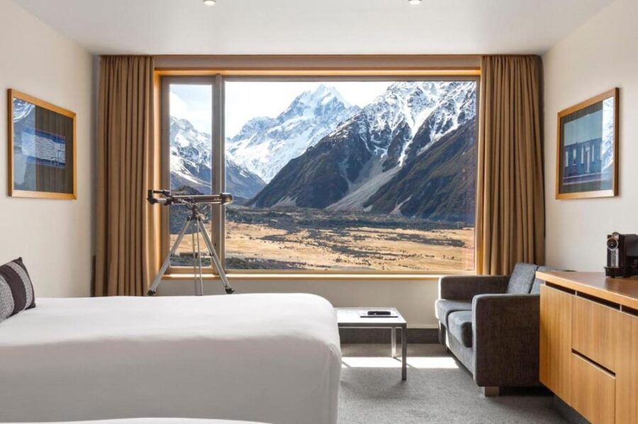 Luxury mountain view hotel room with telescope, modern decor, and panoramic snow-capped alpine peaks.