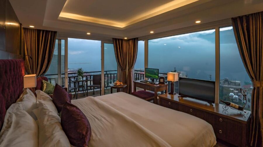 Luxury mountain-view hotel room with plush bed, balcony, panoramic windows, and misty landscape.