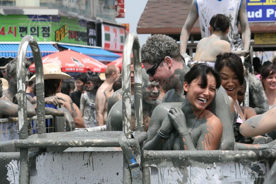Lively mud festival scene with diverse participants enjoying playful mud baths.