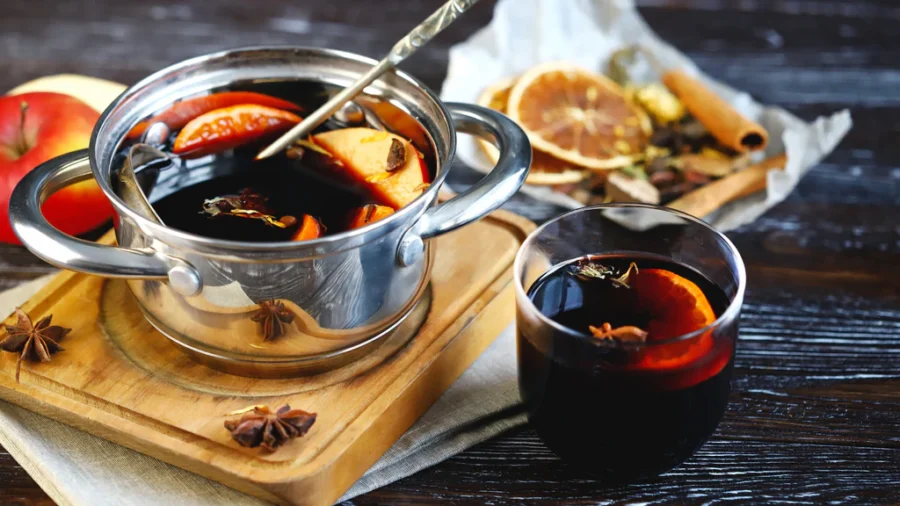 Mulled wine pot with orange slices, star anise, cinnamon sticks and a glass.