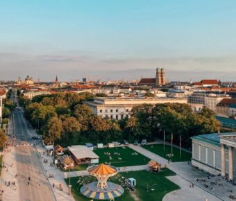 Munich cityscape during golden hour, blending historical and modern architecture, featuring greenery and people.