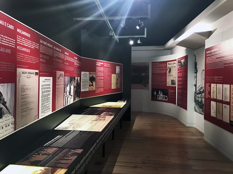 Aljube Museum archival exhibition corridor with red panels and glass-covered display table.