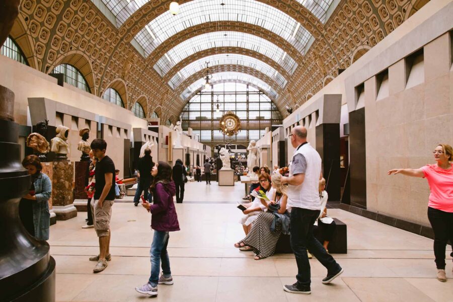 Lively museum interior with diverse visitors, historic architecture, and artworks under natural light.