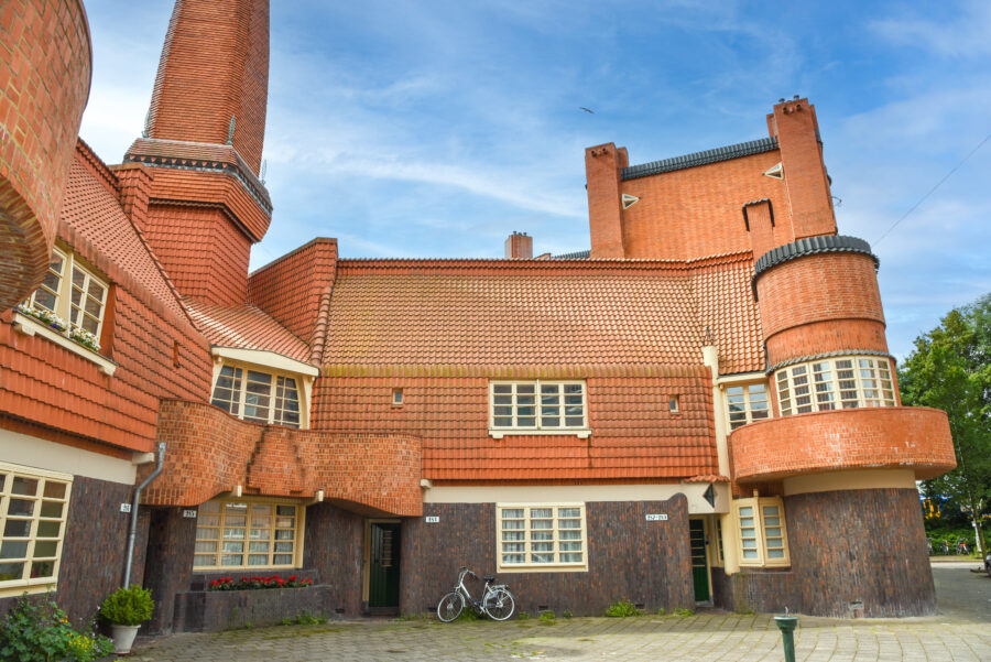 Residential building in Amsterdam featuring a brick chimney and a bike parked in front, showcasing The Amsterdam School style