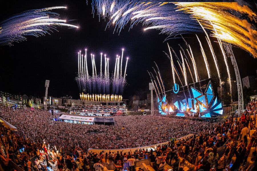 Large crowd at electrifying night music festival with fireworks and dynamic stage lighting.