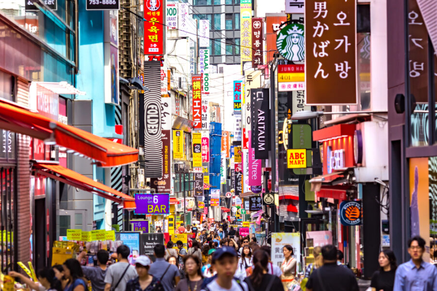 Bustling Myeongdong, Seoul street with shops, neon signs, diverse crowd, urban energy.