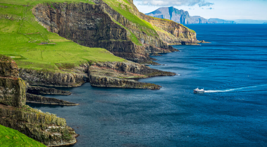 Boat travels through the water, nearing Mykines Island in the picturesque Faroe Islands.
