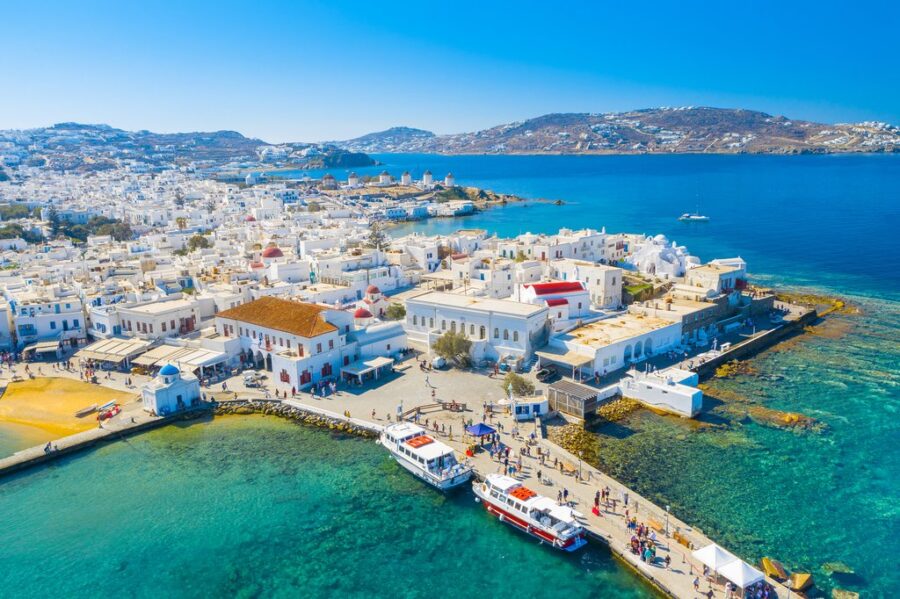 Aerial view of Mykonos, capturing Mediterranean architecture, blue waters, sailboats, and vibrant culture.