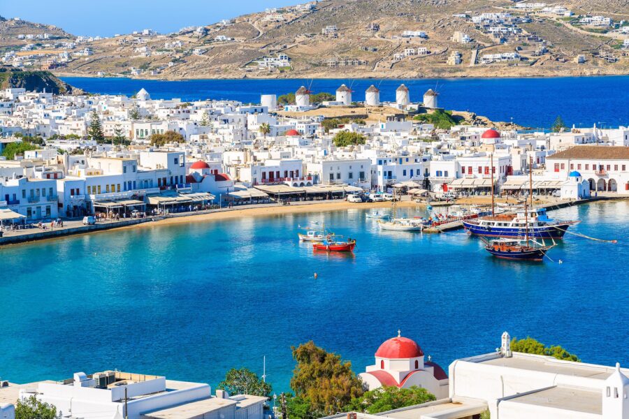Beautiful Mykonos bay with boats, whitewashed buildings, windmills, and clear blue sky.