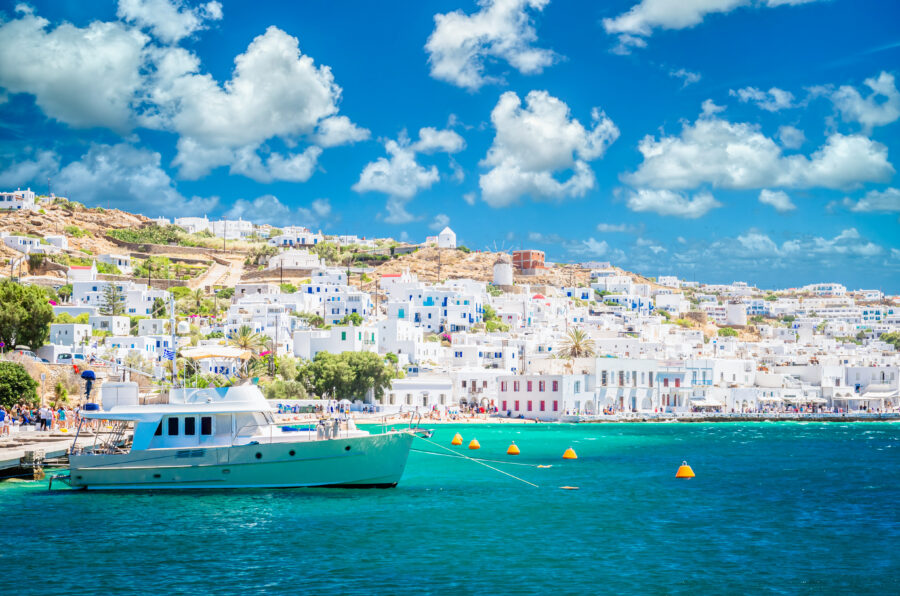 Scenic view of Mykonos town featuring white houses and boats in the old harbor, set against a clear blue sky