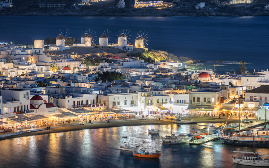 Night view of Mykonos windmills illuminated against a dark sky, showcasing their iconic silhouette and charm