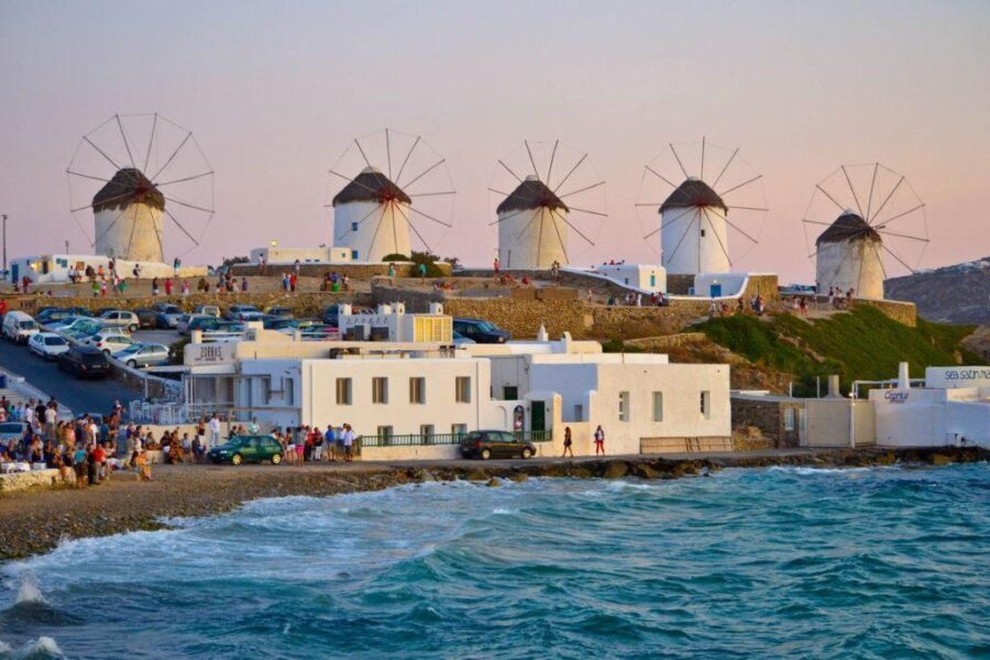 Mykonos sunset: iconic white windmills, azure sea, rocky shoreline, and vibrant coastal charm.