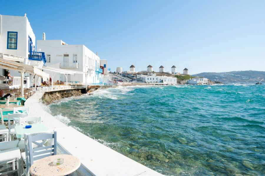 Mykonos Town, Greece, featuring iconic white buildings and a traditional windmill against a clear blue sky