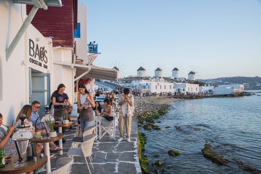 Sunset at Mykonos waterfront with cocktail bar, windmills, and vibrant atmosphere.