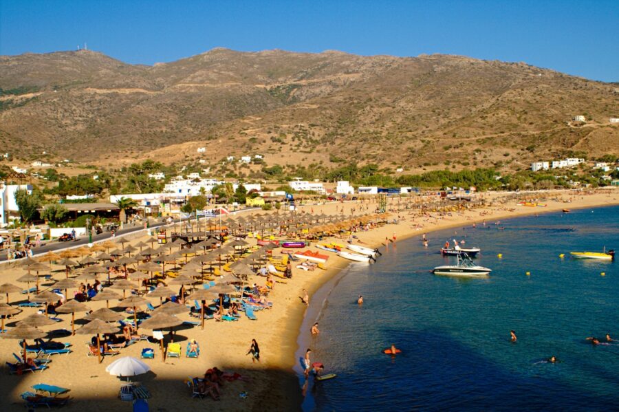 Beach chairs and colorful umbrellas line Mylopotas Bay on Ios Island, surrounded by clear blue waters and sandy shores