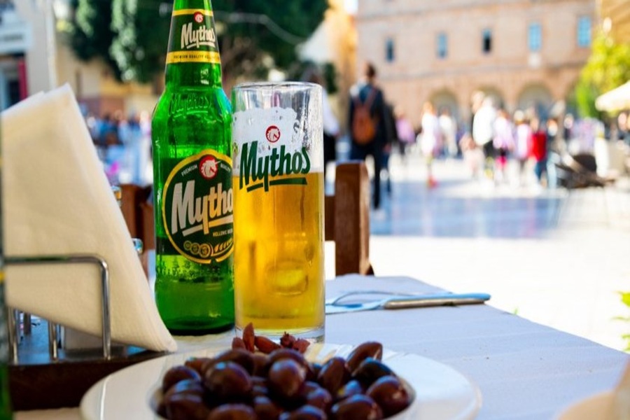 Chilled Mythos beer and olives in a vibrant Greek plaza setting.