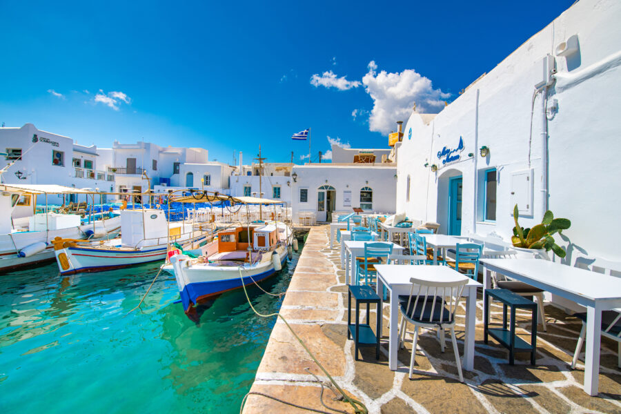 Scenic view of Naousa port in Paros Island, Greece, featuring outdoor tables and vibrant waterfront activity.