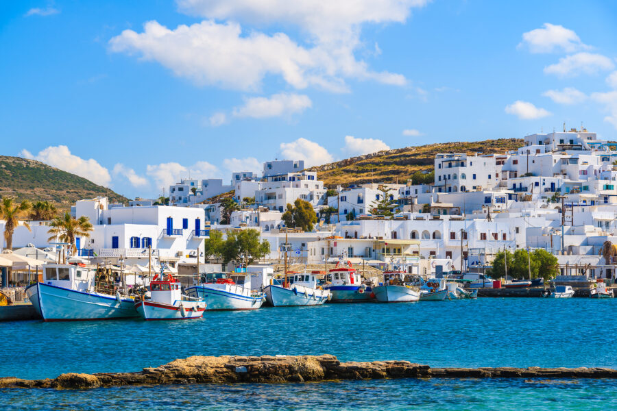 Naoussa port on Paros island, Greece, showcasing white houses and traditional fishing boats against a clear sky.