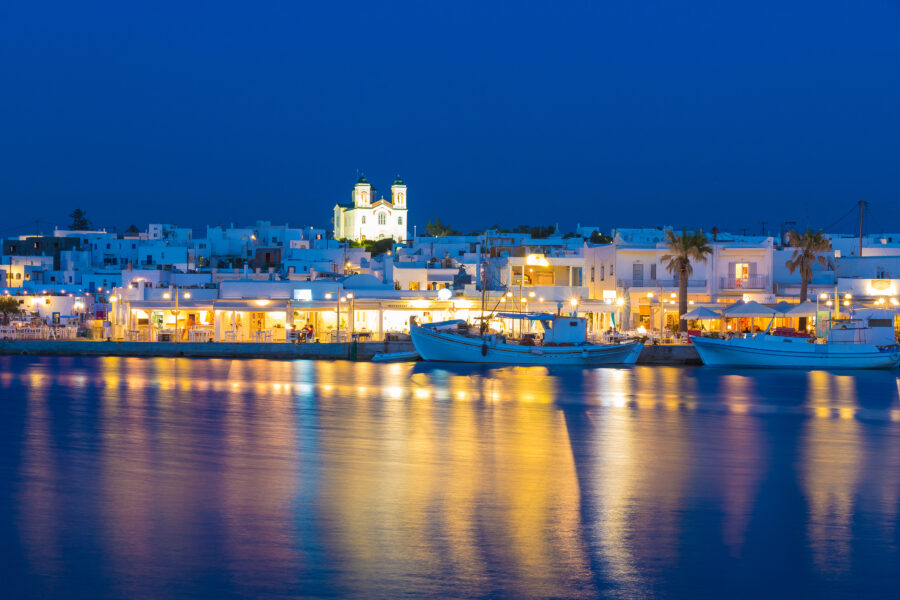 Night view of Naoussa town on Paros island, showcasing illuminated buildings and the serene Aegean Sea.
