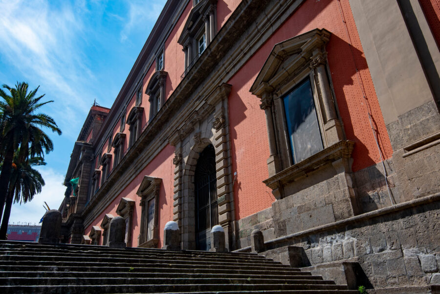 Side view of the Naples National Archaeological Museum showcasing its classical architecture and surrounding landscape.
